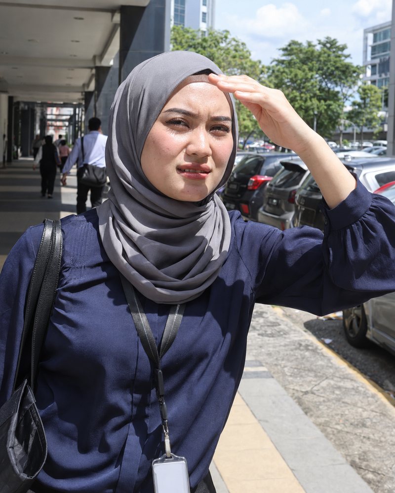 Woman in a tudung squinting and shading her face from the midday sun in KL
